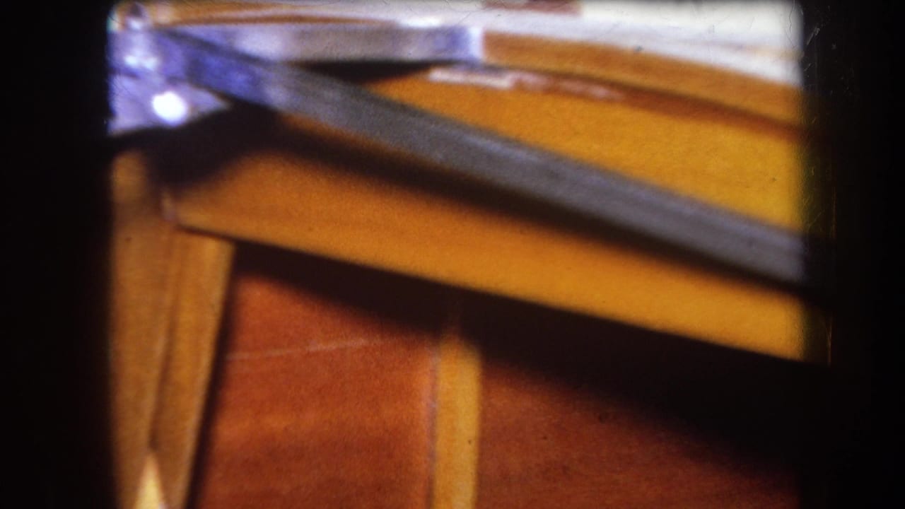 Close 1964 8mm frame of wooden furniture and a dark metal rail, partly obscured by shadow and shallow focus.