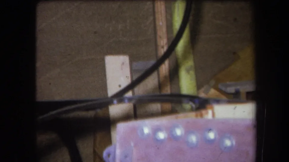 1964 Volmer Yucaipa close-up with a black cable crossing a workshop surface beside wood, metal hardware, and pale circular marks.