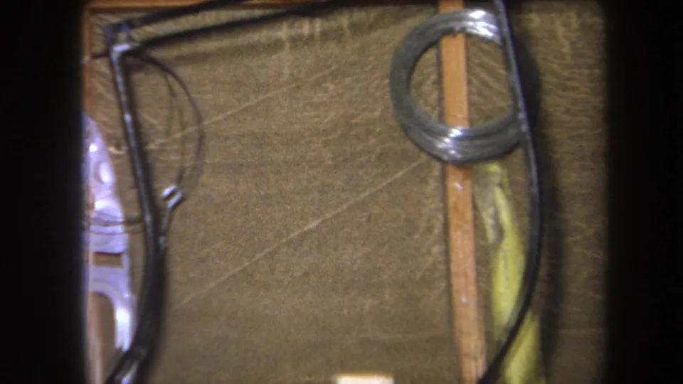1964 Yucaipa 8mm frame with black wiring, a coiled metal spring, vertical wood strips, and textured brown wall material.
