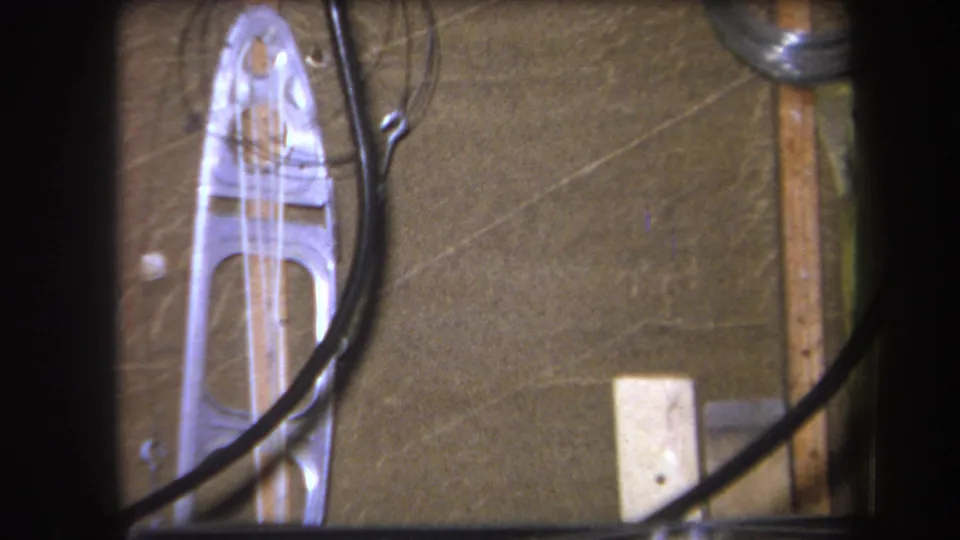 1964 Yucaipa 8mm frame showing a translucent plastic form with openings, black tubing, thin wire, wood strips, and wall texture.