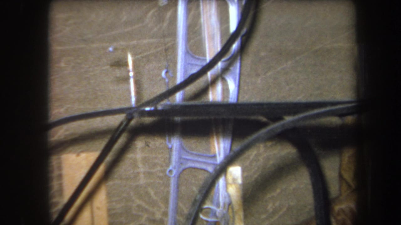 1964 8mm frame from Yucaipa showing black cables draped across unfinished wood framing and a pale metal support bracket.