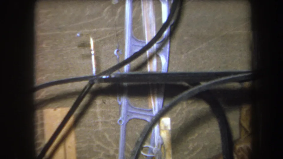 1964 8mm frame from Yucaipa showing black cables draped across unfinished wood framing and a pale metal support bracket.