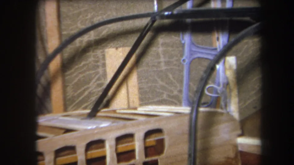 1964 Yucaipa home-movie frame showing exposed black cables over slatted wood and unfinished wall material in an interior workspace.