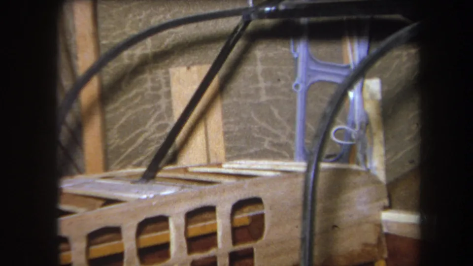 1964 8mm frame from Yucaipa with black wiring curving across wooden framing, wall material, and a pale metal bracket.