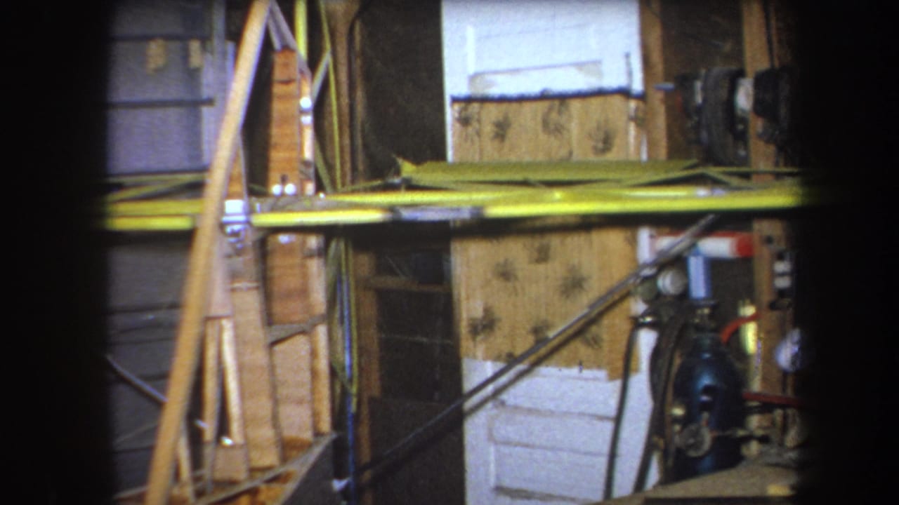 1964 Yucaipa-area 8mm frame showing a wooden aircraft structure with yellow wing surfaces in a private garage or hangar interior.