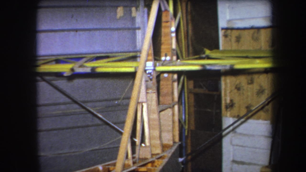 Home-movie frame from the 1964 Yucaipa metadata shows yellow aircraft wing material and exposed wooden supports against a gray garage door.