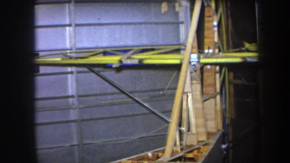 The 8mm frame shows a partially built wooden aircraft section with yellow wing covering and structural bracing inside a private interior.