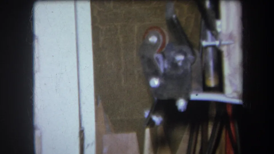 Final 8mm frame shifts to a blurred close view of a wall surface, pale trim, and a small mounted metal fixture or tool at the edge.