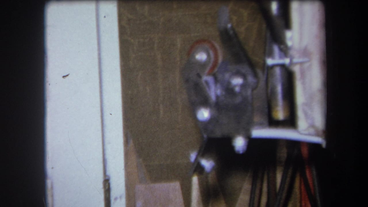 1964 8mm frame from Yucaipa showing a close, soft-focus view of metal workshop hardware near a pale vertical edge.