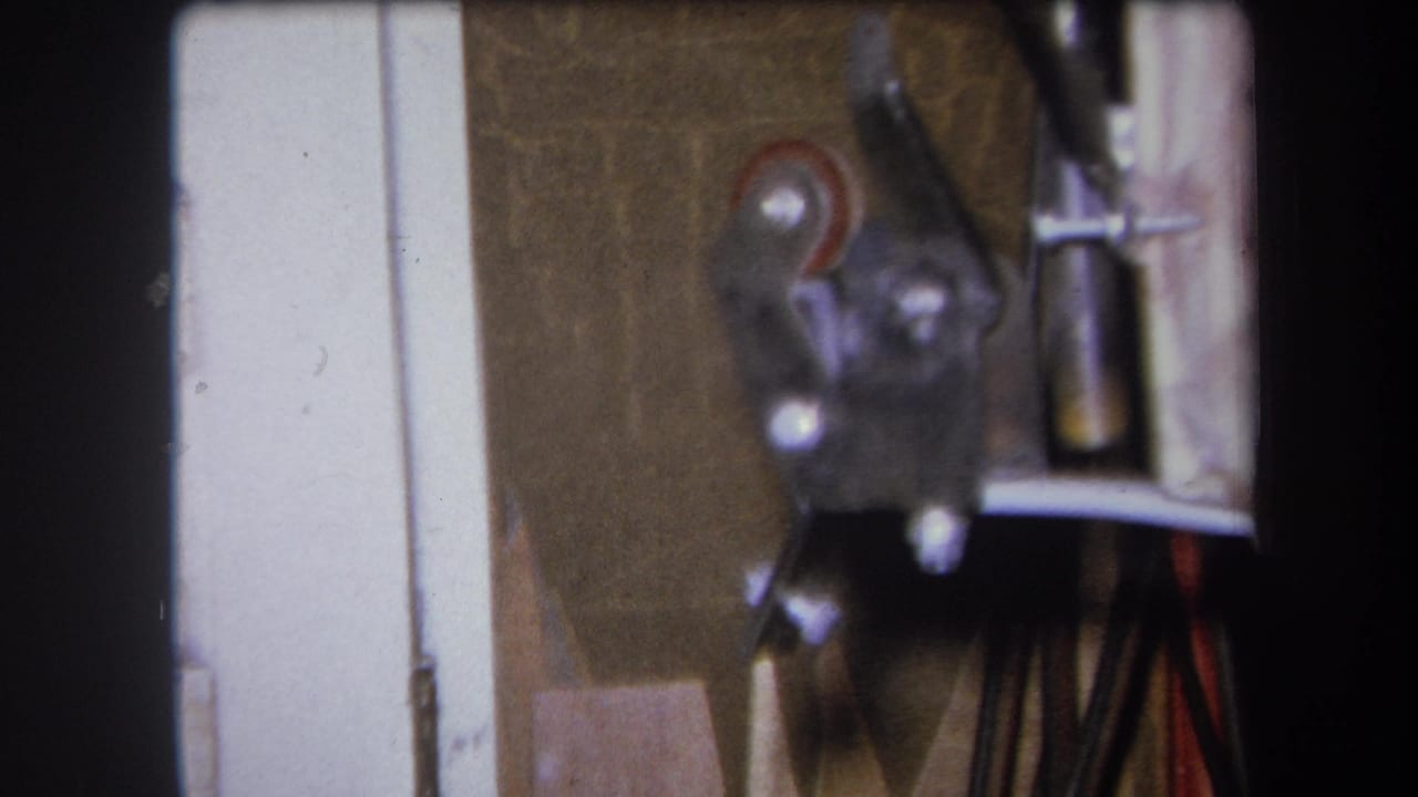 Close view of metal workshop hardware with a small red wheel and vertical parts.