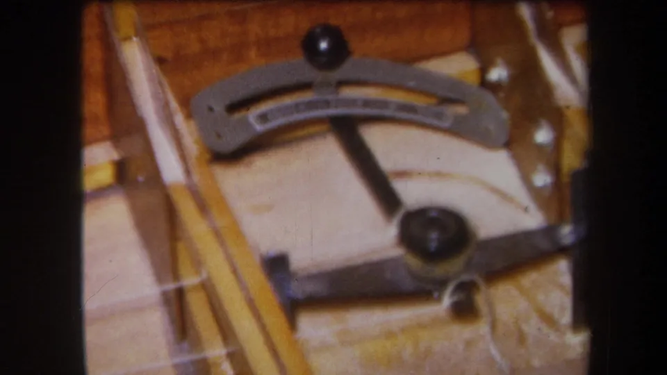 Close 1964 Yucaipa 8mm view of a curved workshop gauge with black knobs, metal arms, and warm wood tones.