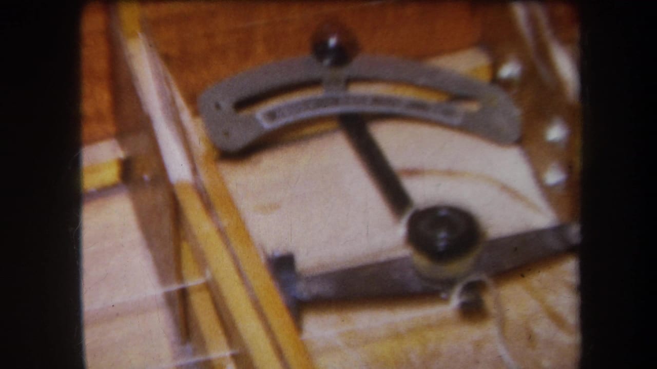 1964 8mm close-up from Yucaipa showing a wooden stringed instrument frame with a curved metal lever, tuning hardware, and dark adjustment knobs.