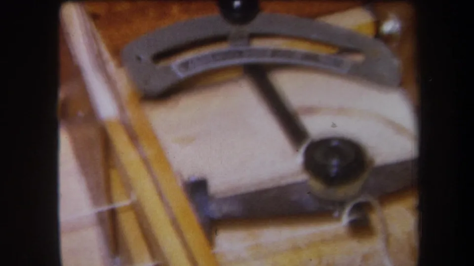 Close 1964 home-movie view of the stringed mechanism, emphasizing the dark knob, metal lever, strings, and warm wooden mounting surface.