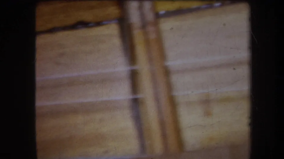 Final 1964 8mm frame shows a softer view across the wooden stringed frame, with parallel strings and hardware receding out of focus.