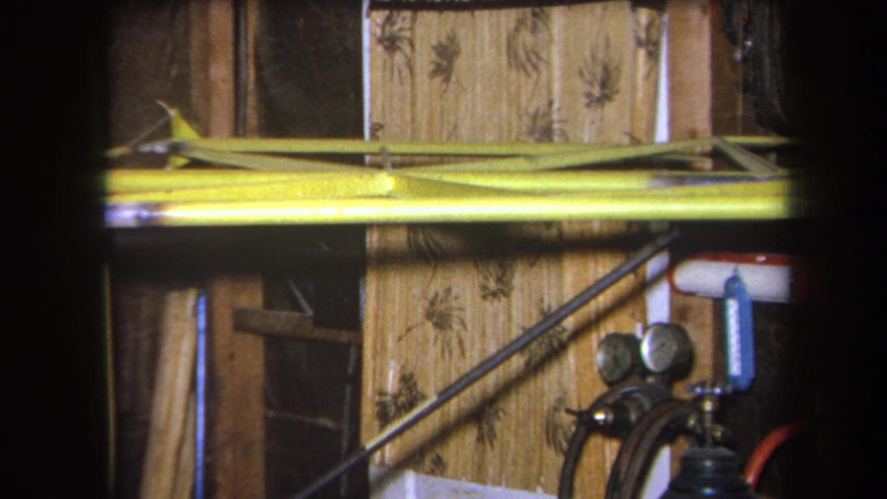 1964 Volmer Yucaipa 8mm frame showing yellow metal equipment, analog pressure gauges, hoses, pipes, and a patterned wall surface.