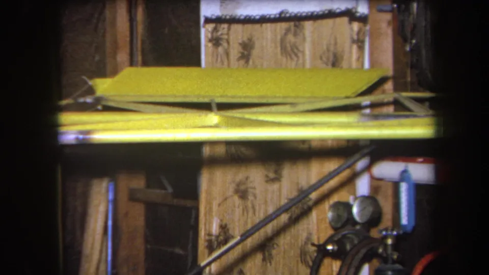 1964 Volmer Yucaipa home-movie frame with a yellow metal rail or conduit above pressure gauges and hoses against a wood and patterned wall.