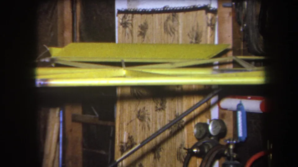 1964 Volmer Yucaipa 8mm frame showing a close workshop detail with yellow metal framing, pressure gauges, hoses, and wood wall surfaces.