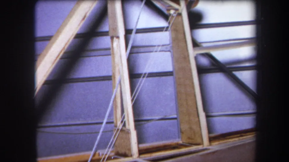 1964 Yucaipa home-movie frame showing wooden bracing, white cables, and metal rods in a warehouse-like interior.
