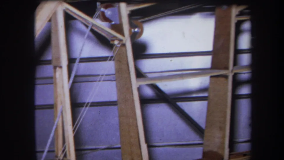 1964 Yucaipa home-movie view of angled wood bracing, cable lines, and metal rods in a warehouse-like interior.