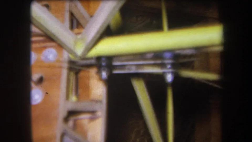 End frame from 1964 8mm footage with a soft close-up of yellow metal work, bolts, and timber bracing.