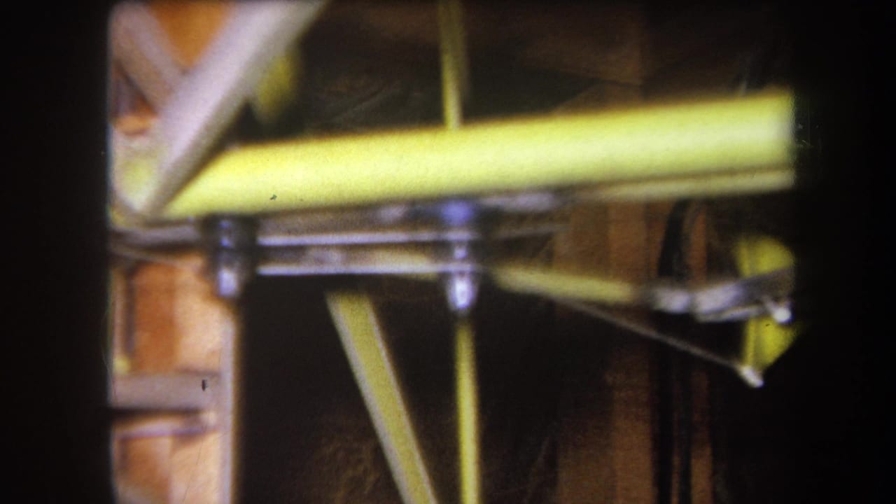 1964 Yucaipa 8mm frame showing yellow-painted steel members, bolted brackets, and exposed wood supports in close view.