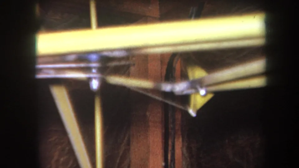 Close 1964 construction detail with yellow-painted steel reinforcement, metal fasteners, and exposed wooden backing.