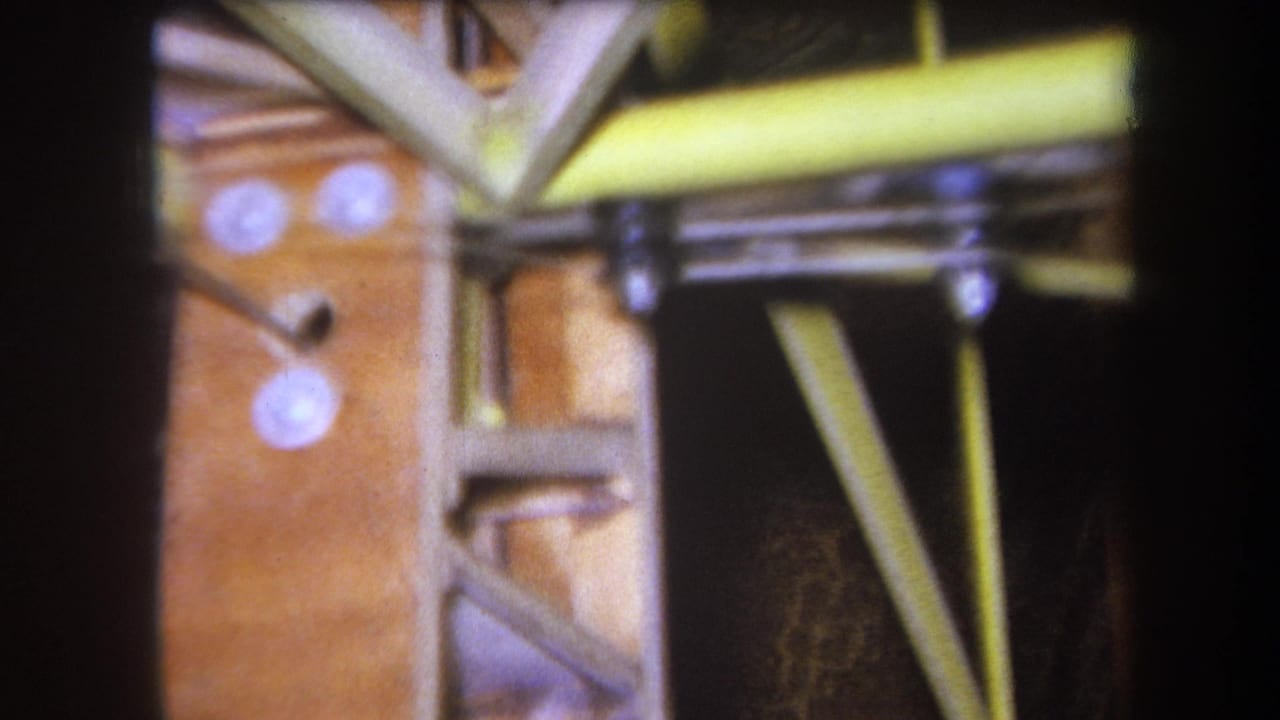 1964 Yucaipa 8mm close-up showing a wooden structural panel, diagonal braces, yellow rods, and round white fasteners.