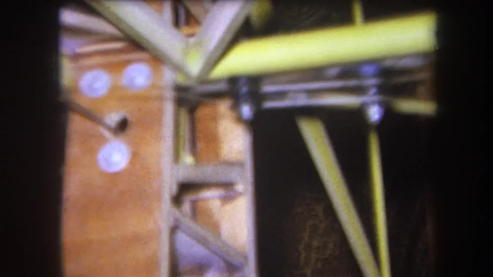 1964 Yucaipa 8mm close-up showing a wooden structural panel, diagonal braces, yellow rods, and round white fasteners.