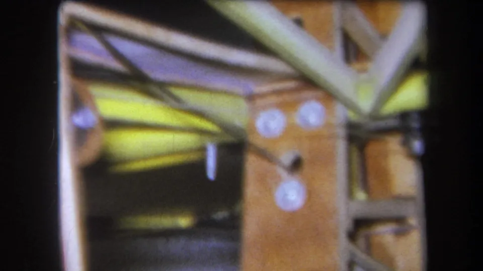 1964 Yucaipa home-movie frame showing a close mechanical detail with wood, metal struts, yellow rods, and white circular fasteners.