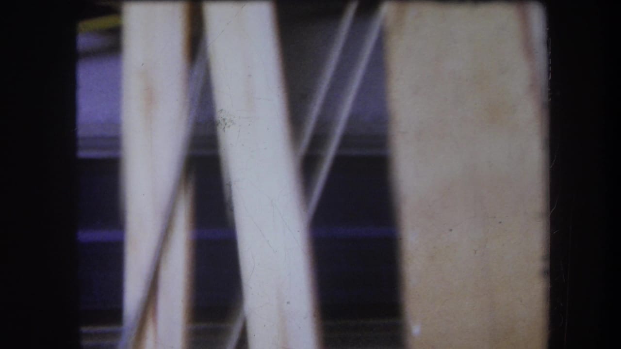 Close-up of pale vertical supports and dark background around a wooden mechanical setup.