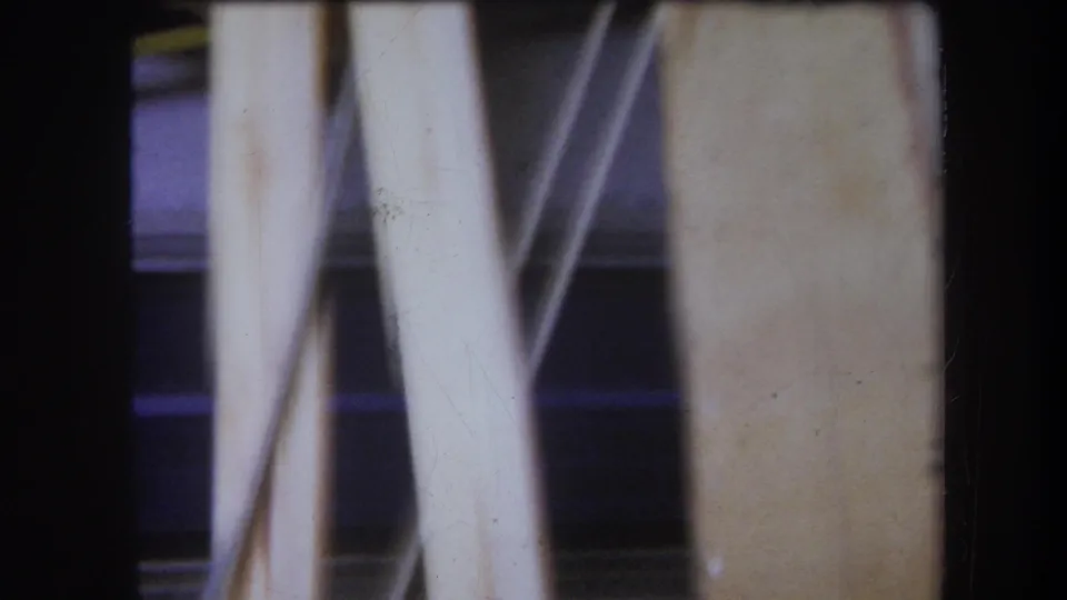 1964 8mm frame from Yucaipa showing pale supports and part of a wooden textile or winding apparatus in soft focus.