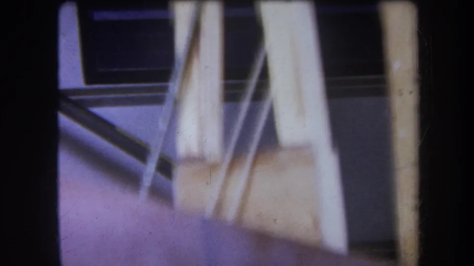 1964 Yucaipa home-movie frame with pale supports, angled rods, and a blue-toned background around the spool apparatus.