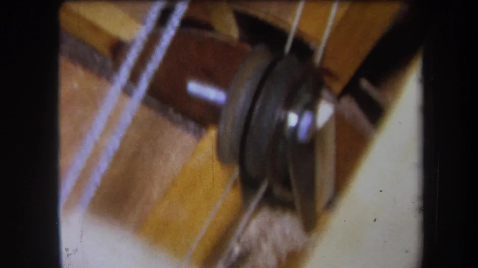 Close-up from the 1964 Yucaipa 8mm clip showing a metal disc, white yarn, and wooden boards in the winding mechanism.
