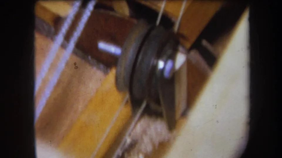 Yucaipa 1964 home-movie frame of pale thread crossing a dark pulley and worn sewing-machine assembly.