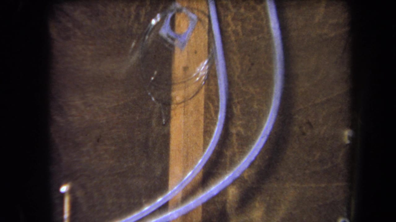 1964 Yucaipa-area 8mm frame showing a wooden board, clear coiled tubing, and a small plastic fitting in close-up.