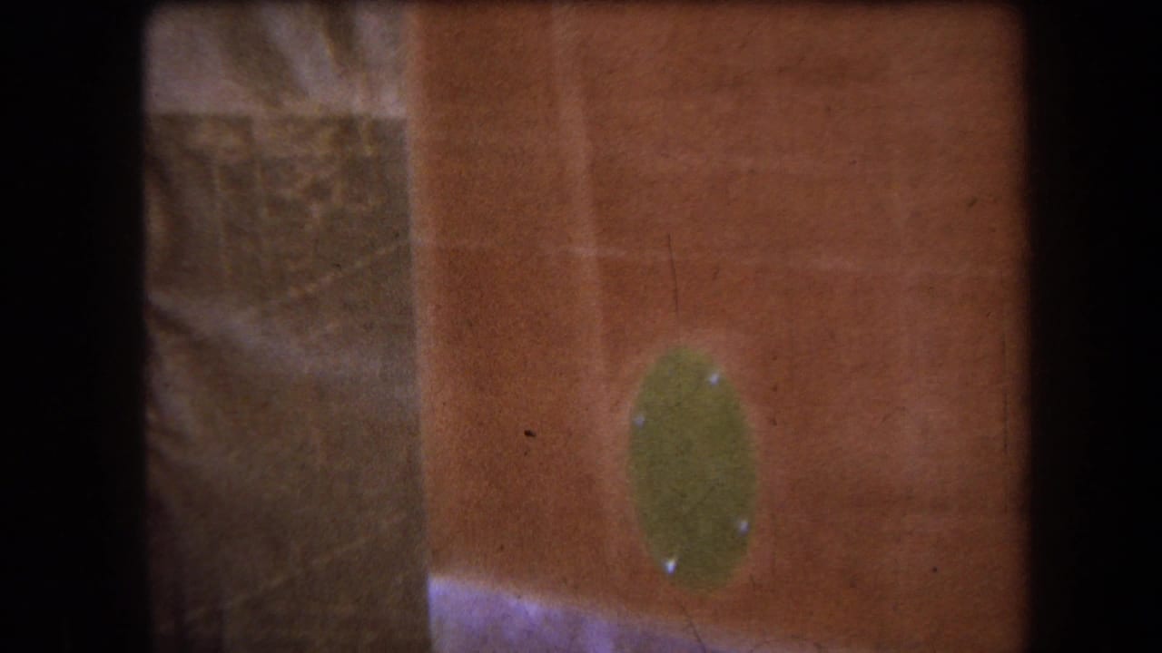 1964 8mm frame from Yucaipa metadata showing a close reddish painted hull-like surface with a green oval fitting and dark film edge.