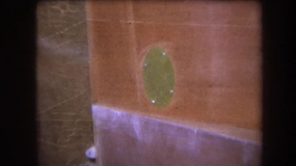 Close 1964 home-movie view of the painted vessel-like surface, with a green oval fitting and pale trim band in soft focus.