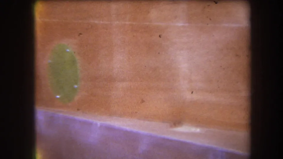 The 8mm frame shows the camera panning past a green oval fitting on a warm reddish hull-like surface with visible film wear.