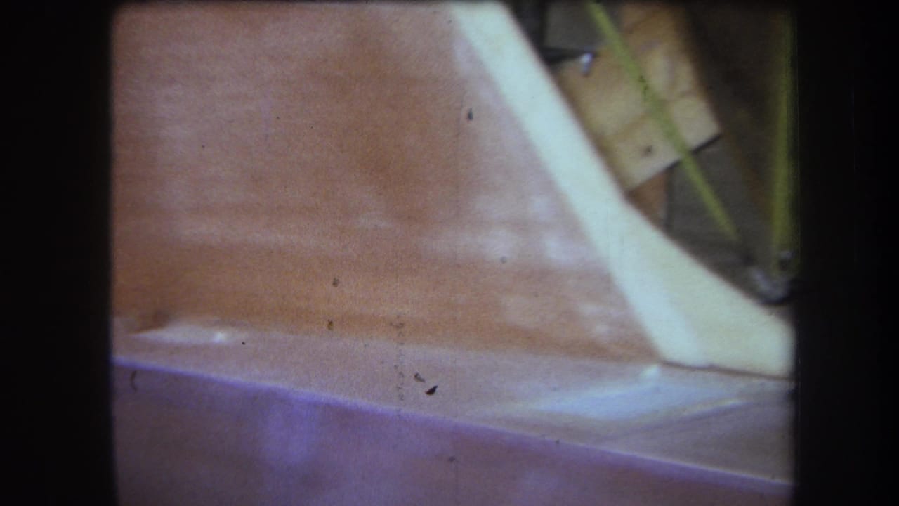 1964 Yucaipa-area 8mm frame showing a close, partial view of a reddish surface, pale curved edge, and yellow metal object.