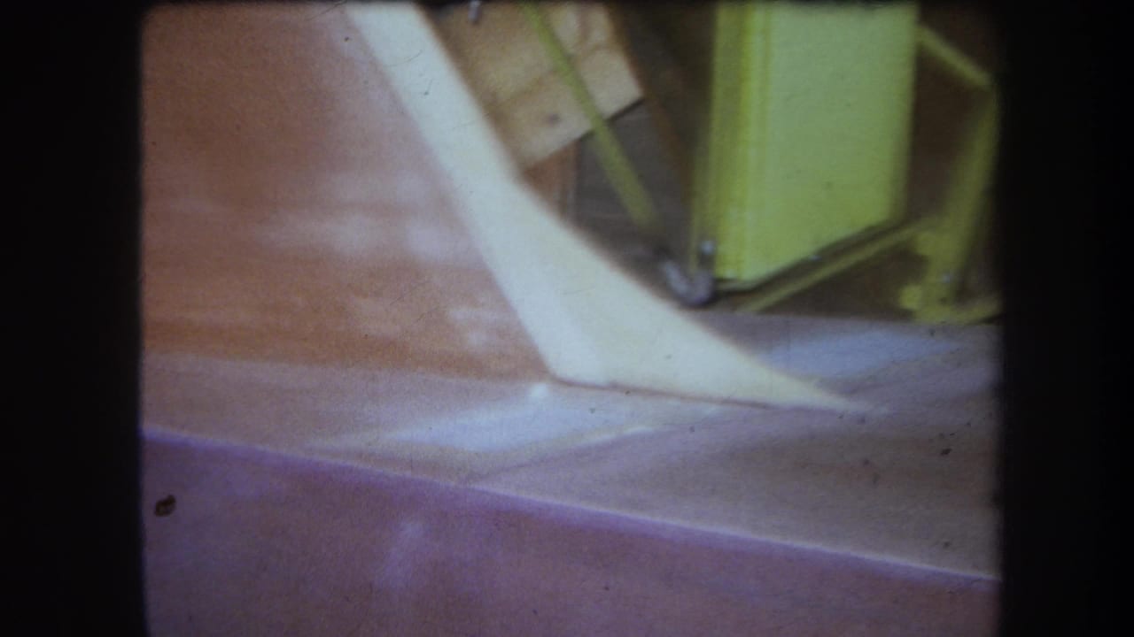 Pale curved edge beside a reddish surface with a yellow metal frame in the background.