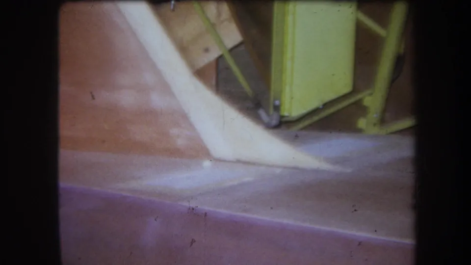 1964 Yucaipa-area 8mm close-up showing a yellow metal object, pale curved strip, and reddish-brown surface.