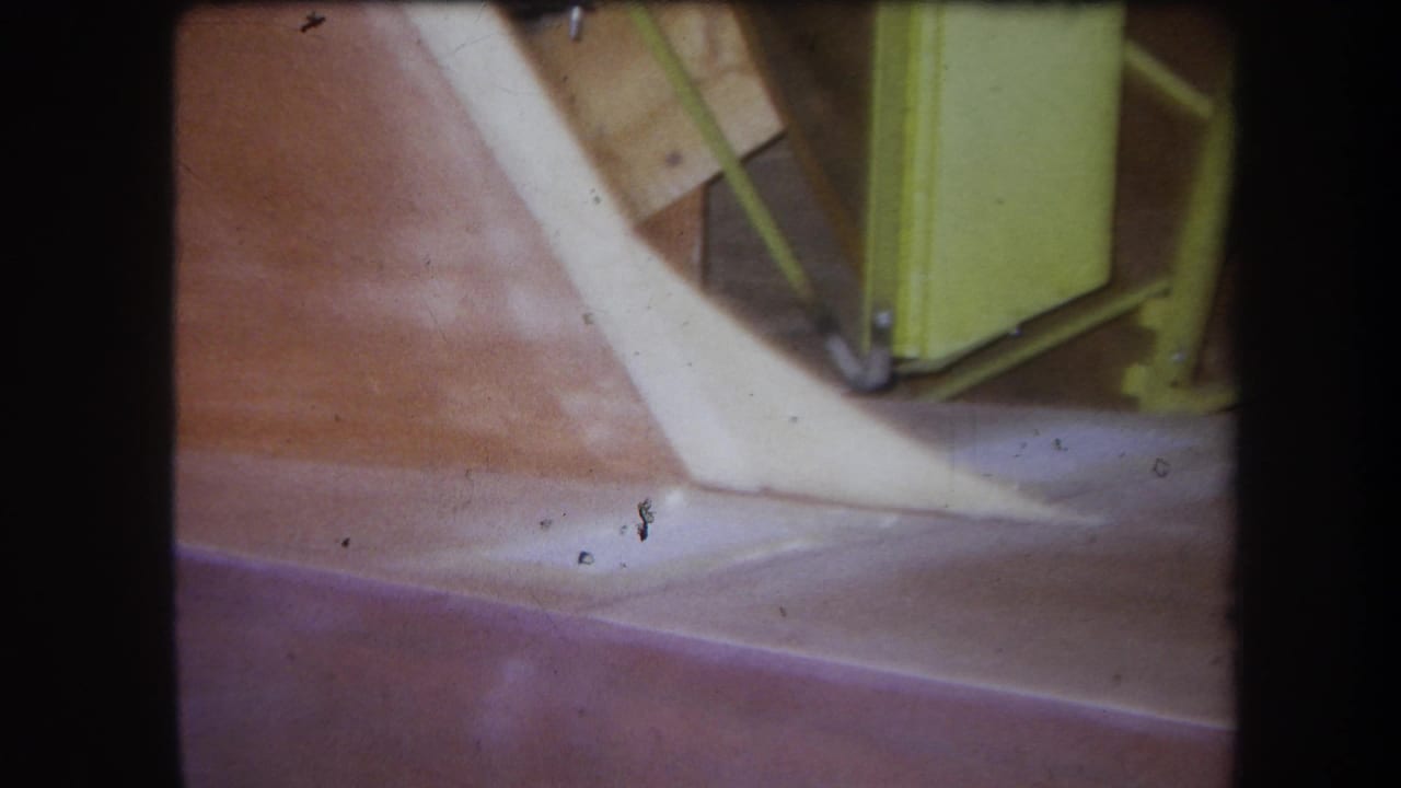 1964 Yucaipa 8mm frame showing close agricultural equipment details, including a reddish surface, pale angled component, and yellow-green metal frame.