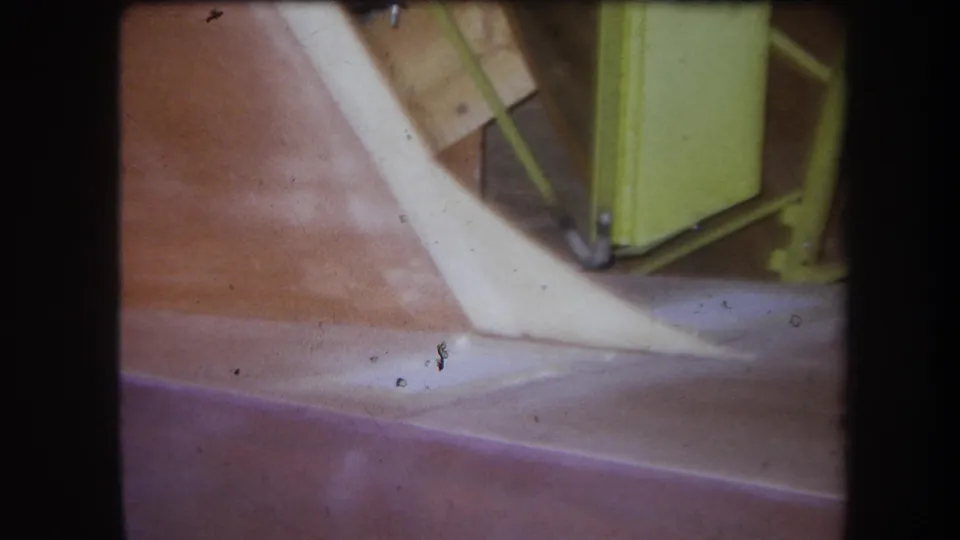 1964 Yucaipa 8mm frame showing close agricultural equipment details, including a reddish surface, pale angled component, and yellow-green metal frame.