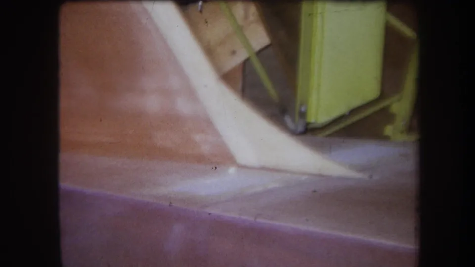 1964 Yucaipa 8mm close-up of an old agricultural machine section with a pale angled part and yellow-green frame above a reddish surface.