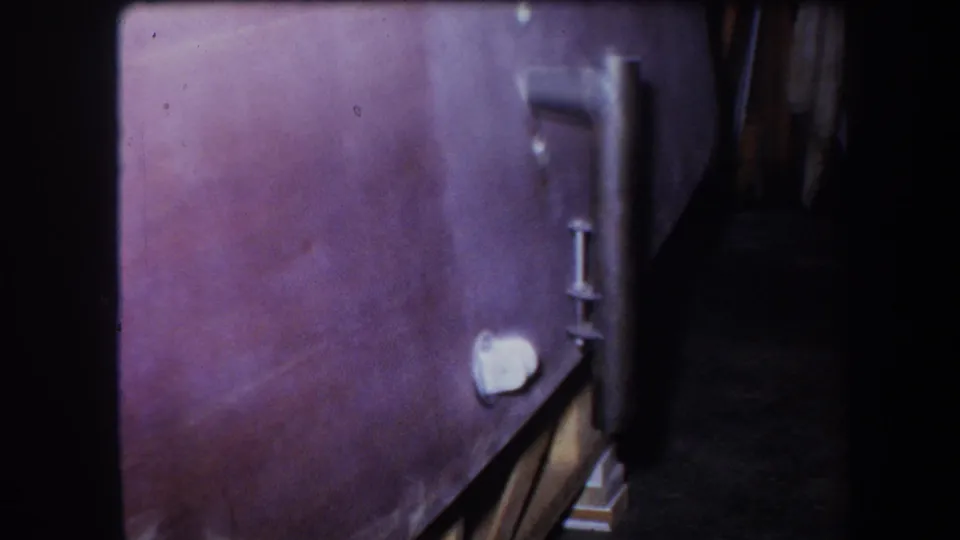 1964 Yucaipa 8mm frame showing the side of agricultural equipment with a vertical metal fitting, small pale knob, and dark recessed area.