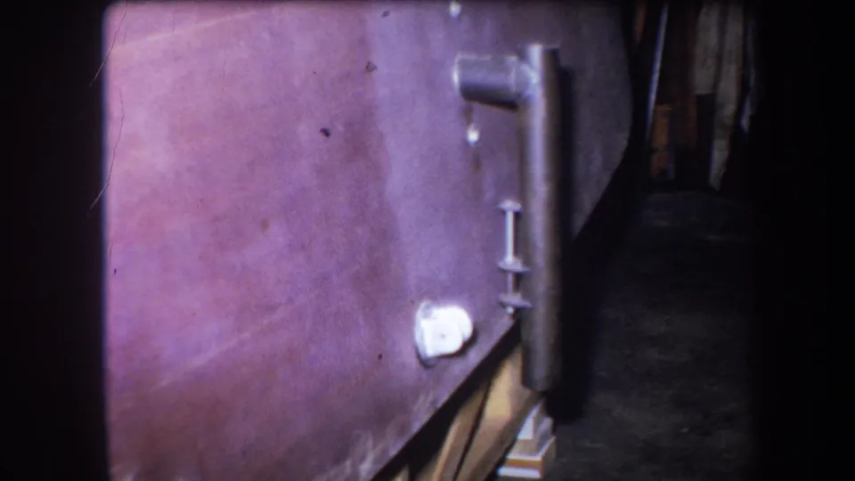 1964 8mm frame from Yucaipa showing a close-up of an old boiler side, vertical pipe, handle and white circular fitting in a dim utility space.