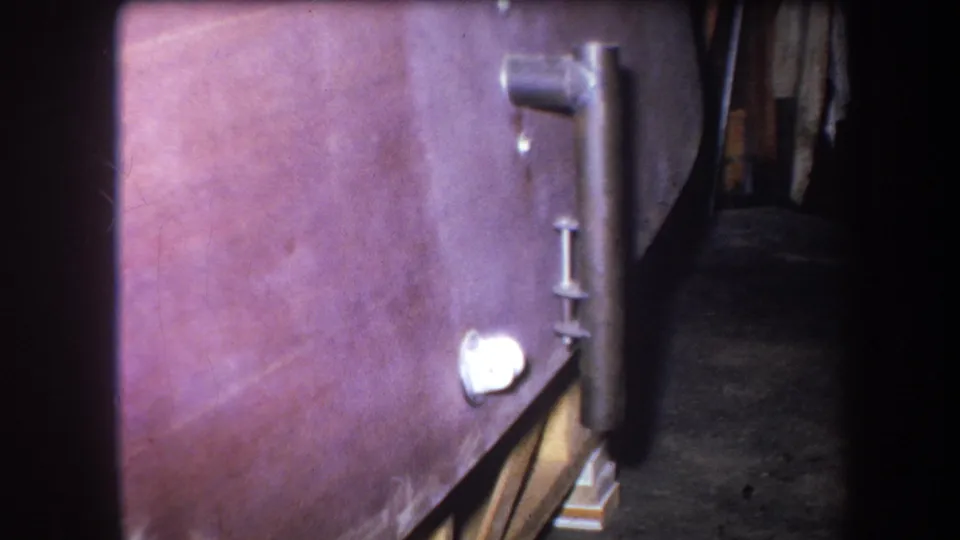 Soft 8mm frame from 1964 Yucaipa showing the boiler side, attached vertical pipe and white circular fitting with a shadowed floor beside it.