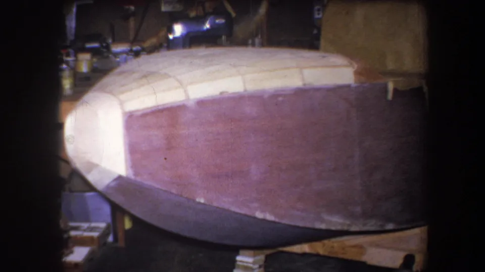 1964 Volmer Yucaipa 8mm frame showing the unfinished hull on wooden supports, with tools and materials partly visible in the workshop.