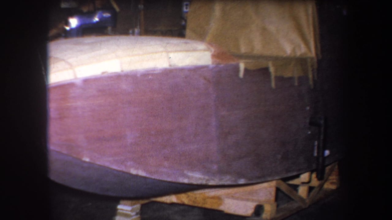 Close 1964 home-movie view of the brown and pale wooden boat hull resting in a Yucaipa workshop.