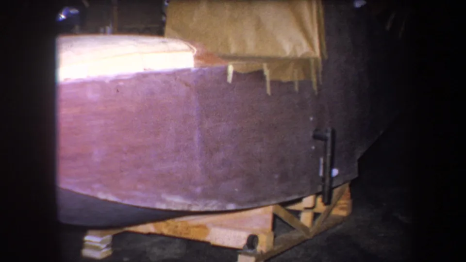 1964 Yucaipa workshop frame showing the side of a wooden boat hull on a rough support structure.